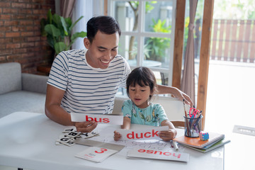 portrait of father teaching toddler how to read by using simple word and letter on a flash card at...