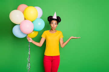 Photo of pretty dark skin lady holding many air balloons and new sale price product offering buy wear casual yellow t-shirt red pants and paper cap isolated green background