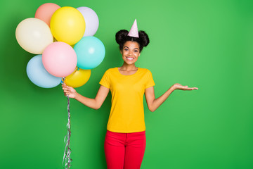Photo of pretty dark skin lady holding many air balloons and new sale price product offering buyers credit wear casual yellow t-shirt red pants and paper cap isolated green background