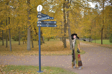 young beautiful pretty lady woman posing in a long green and brown dress gown overcoat walks down a lonely alley in the garden and looks at the information sign with emotions