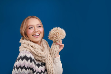 Young woman in warm sweater and scarf on blue background, space for text. Winter season