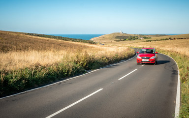 Road Trip; South Downs, England. A car travelling a winding road in East Sussex with Belle Tout...