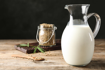 Composition with pitcher of hemp milk on wooden table against black background. Space for text