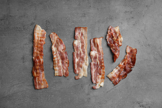 Slices of tasty fried bacon on dark background, flat lay