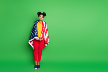 Full body photo of pretty dark skin lady celebrating independence usa day holding national flag on parade like coast wear casual yellow t-shirt red pants isolated green background