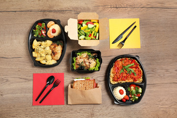 Lunchboxes with different meals on wooden table, flat lay. Healthy food delivery