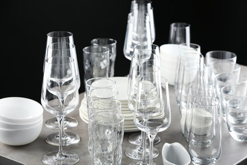 Set of empty glasses and dishware on table against black background
