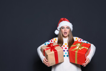 Emotional young woman with Christmas gifts on dark background. Space for text