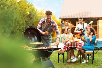 Group of friends at barbecue party outdoors. Young man near grill - obrazy, fototapety, plakaty