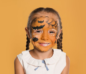 Cute little girl with face painting on orange background