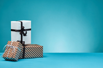 Different sizes, colorful, striped and plain paper gift boxes tied with ribbons and bows on a blue surface and background. Close-up, copy space.