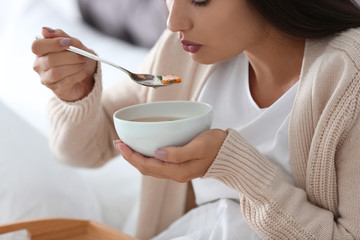 Sick young woman eating soup to cure flu at home