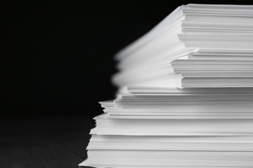 Stack of blank paper on table against black background, closeup