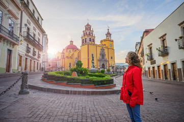 A woman in Guanajuato, a colonial city of Mexico watching a church and sunrise with a red jacket