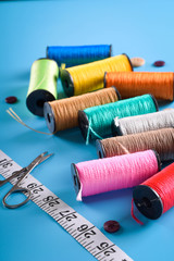 Sewing kit: scissors, measuring tape, thimbles, threads and buttons. Composition with threads and sewing accessories on blue background Colored thread coils on blue background, sewing, place for text
