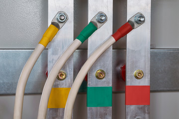 Three electric cable is connected to the vertical aluminum busbars in the electrical control panel by means of bolted connectors. Cables and busbars are color-coded. Electricity distribution.