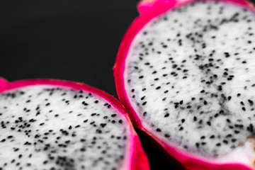 Obraz premium Dragon fruit. Vibrant Dragon Fruit on black background. Sliced white dragon fruit or pitaya on black plate on the table, close-up. Tropical and exotic fruits. Healthy and vitamin food concept.