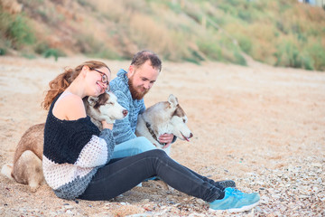 Couple of lovers sitting on the sand on the beach with husky dogs