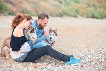 Pair of lovers sitting on the sand on the beach with husky dogs