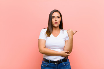 young pretty hispanic woman looking astonished in disbelief, pointing at object on the side and...