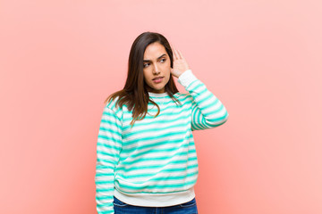 young pretty hispanic woman looking serious and curious, listening, trying to hear a secret...