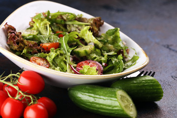 bowl of salad with vegetables and greens, with tomato, cucumber and onions on rustic table