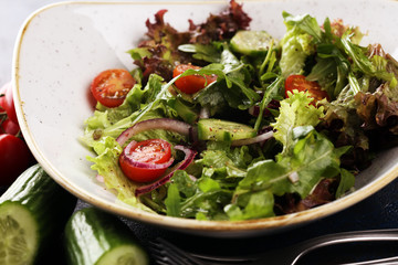 bowl of salad with vegetables and greens, with tomato, cucumber and onions on rustic table