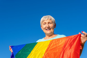 smiling senior woman with lgbt flag on blue background