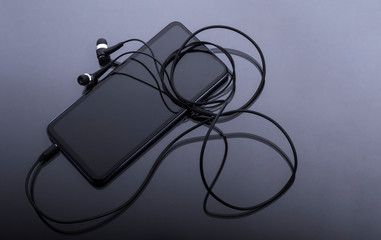 black smartphone with black headphones on glass surface
