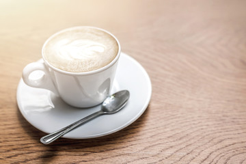 White cup of coffee with art on wooden table with copy space.