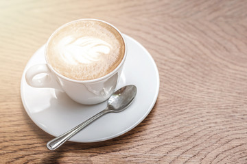 White cup of coffee with art on wooden table with copy space.