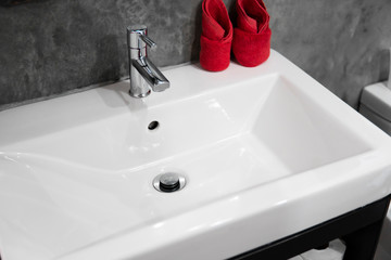 Modern stainless steel faucet with wash basin sink with a two red towels on it . Counter bathroom interior contemporary. Luxury and stylish design bathroom with a concrete style walls.