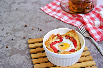 Breakfast, baked egg with cheese, sweet pepper and bread in a white portion form on a gray concrete background.