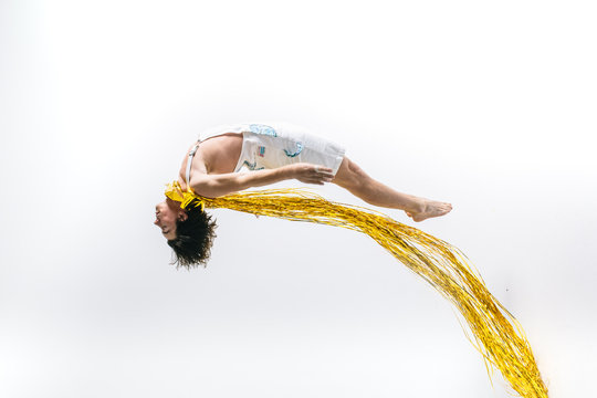 Male dancer jumps into the air with shiny gold streamers as a cape