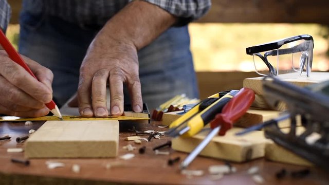 Adult carpenter craftsman takes the measure and with the carpenter's square trace the cutting line on a wooden table. Construction industry, housework do it yourself. Footage.