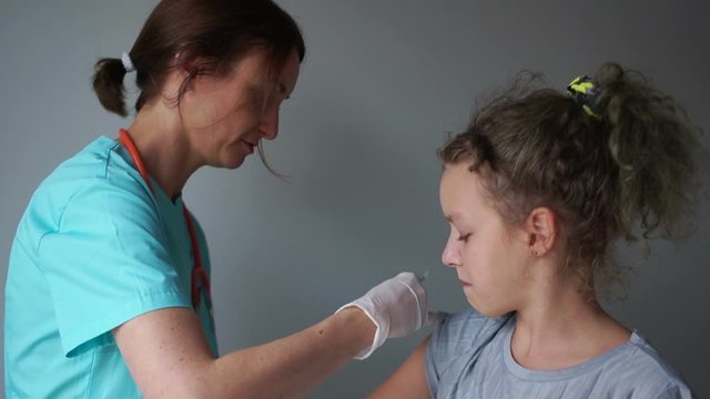 Nurse in a medical suit gives a flu shot to a teenage girl in a medical room. Flu vaccine, medical manipulation