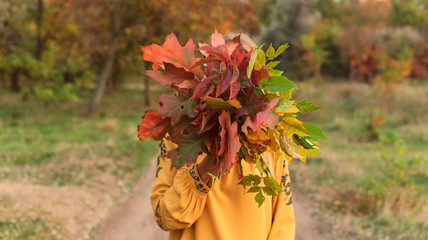 Beautiful blonde covering her face by armful of leaves in autumn park