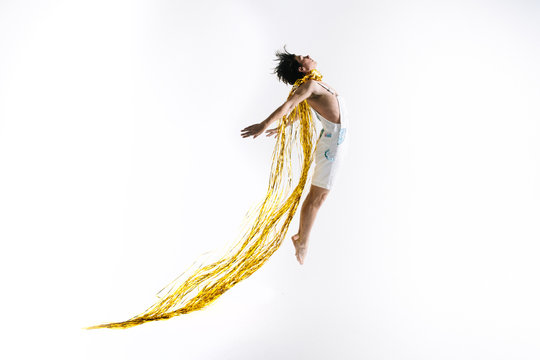 Male dancer jumps into the air with shiny gold streamers as a cape