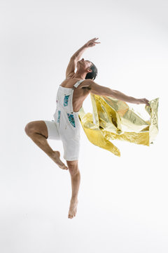 Male dancer leaps into the air with reflective gold cape