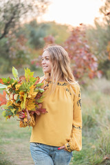 Beautiful blonde with an armful of leaves in autumn park