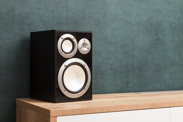 Single modern black audio speaker in interior on wooden desk near the wall