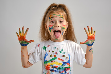 Little girl in white t-shirt is posing standing isolated on white and gesticulating with her painted in different colors palms. Art studio. Close-up. - obrazy, fototapety, plakaty