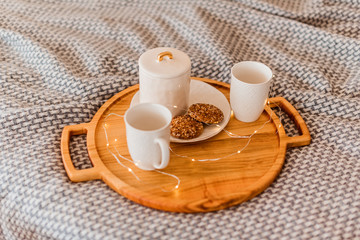 Two cup and cookie on wood tray on bed close up