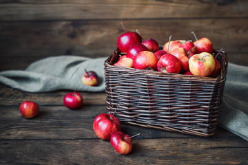 Small red apples in a wicker box on a dark wooden background.