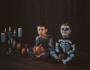 Good little friends in Halloween costumes are sitting on the floor with pumpkins and candles.