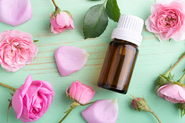 Rose essential oil in glass bottle and flowers on green wooden table.