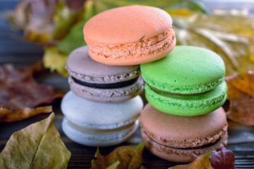 Delicious autumn macaroons next to autumn leaves similar in color lie on the table