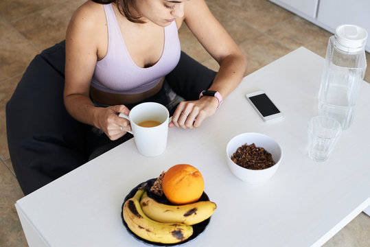 Healthy fitnesswoman looking at smartband while breakfasting.