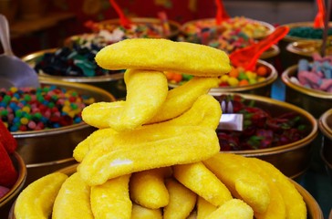 Close up of pile of sweets in shape of yellow banana with blurred bowels filled with sweet candies background on French market - St. Tropez, France