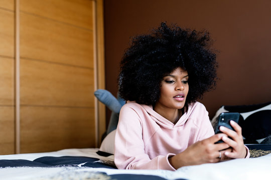 Beautiful afro woman using the mobile in bedroom